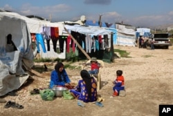 FILE - Syrian women prepare food for their family outside their tents, at a Syrian refugee camp in the town of Bar Elias, in Lebanon's Bekaa Valley, March 29, 2016.