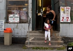 An anti-violence sign, created by former gang members, hangs on a window of a corner convenience store where woman and her daughter finished shopping, Aug. 21, 2017, in the South Side neighborhood of Syracuse, N.Y.