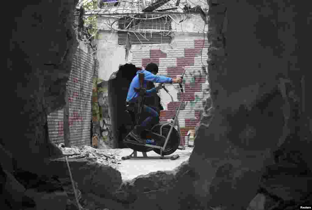 A Free Syrian Army fighter exercises as he is seen through a hole in a wall in the Seif El Dawla neighbourhood in Aleppo, Syria. 
