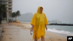 FILE - Maryanne Fisher, of League City, Texas, stands in the rain, Oct. 19, 2014, on Waikiki Beach with Diamond Head in the background in Honolulu as Hurricane Ana brought a steady rain to the Hawaiian Island of Oahu. On Wednesday, NOAA's Central Pacific Hurricane Center announces the hurricane season outlook for 2018. 