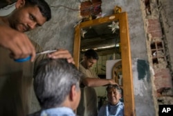 Jorge Flores practices his hairstyling skills on his mother Rosa Vega inside his home, where he is trying to set up a barber shop in the Petare slum, in Caracas, Feb. 14, 2019.