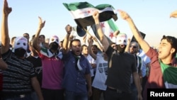 Syrian protesters wave Syrian opposition flags as they shout slogans against Syrian President Bashar Al-Assad outside the Syrian embassy in Amman, July 5, 2012.