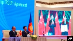 FILE - Vietnamese Prime Minister Nguyen Xuan Phuc, left, and Minister of Trade Tran Tuan Anh applaud next to a screen showing Chinese Premier Li Keqiang and Minister of Commerce Zhong Shan holding up signed RCEP agreement, in Hanoi, Vietnam, Nov. 15, 2020.
