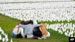 Visitors sit among white flags that are part of artist Suzanne Brennan Firstenberg's temporary art installation to commemorate Americans who have died of COVID-19, on the National Mall in Washington, Sept. 21, 2021. 