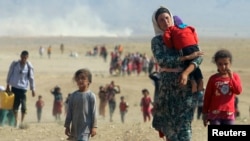 FILE - Displaced people from the minority Yazidi sect, fleeing violence from forces loyal to the Islamic State in Sinjar town, walk toward the Syrian border, on the outskirts of Sinjar mountain, near the Syrian border town of Elierbeh of Al-Hasakah Governorate, Aug. 11, 2014.