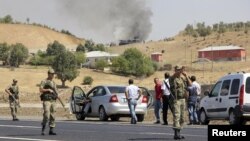 Turkish soldiers take security measures on a main road which connects eastern Turkish cities Bingol and Mus, as smoke rises from a burning vehicle attacked by PKK in the background, September 18, 2012. 