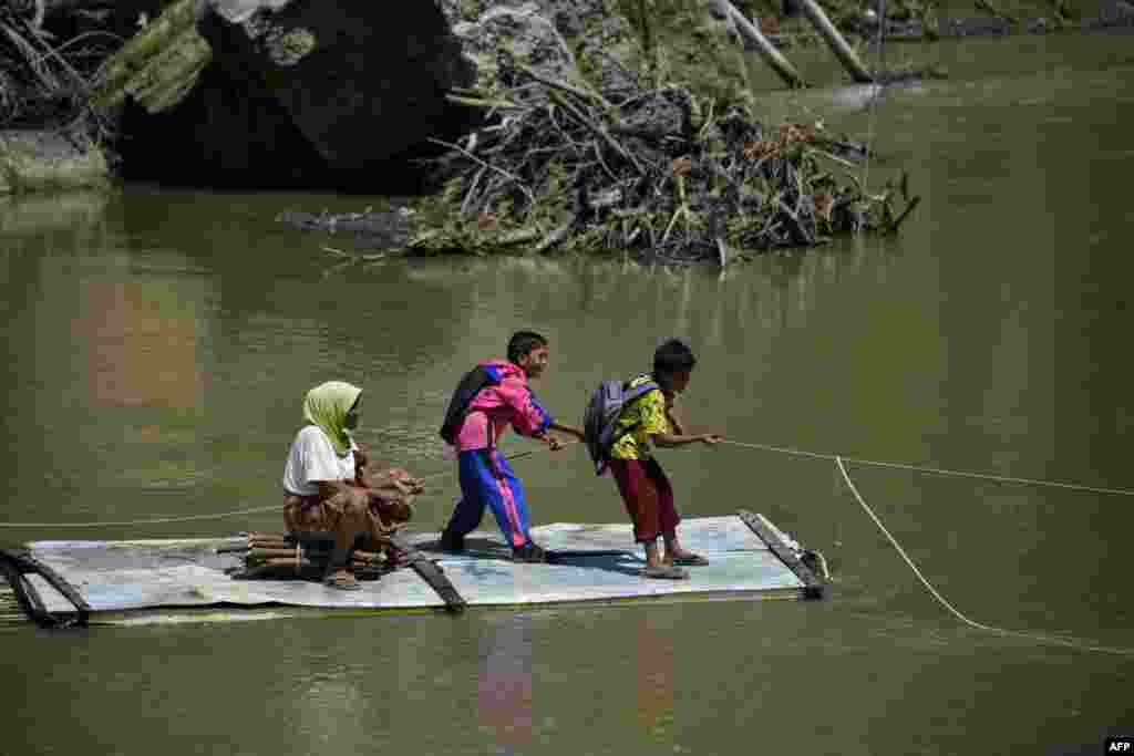 Students pull a rope as they use a bamboo raft to cross a river at a village in Siron, Aceh, Indonesia.