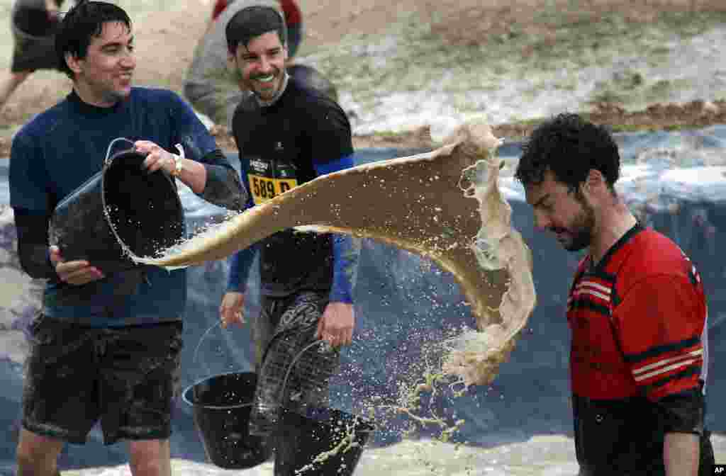 A participant in the Mud Day event throws a bucket of mud at a friend during the Mud Day run in Beynes, west of Paris. Thousands of runners competed in a circuit of approximately 13 kilometers (8 miles) with over 20 obstacles, most of them set in mud.