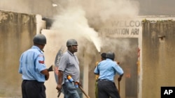 An armed policeman carrying a pistol and tear gas patrols while firemen attempt to put out a fire in the Salvation Army Church after it was set on fire by rioting youths, following Friday Muslim prayers in Mombasa, Kenya, Oct. 4, 2013.