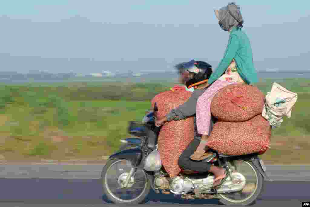 A motorcyclist carries a pillion rider sitting on goods in Phnom Penh, Cambodia.