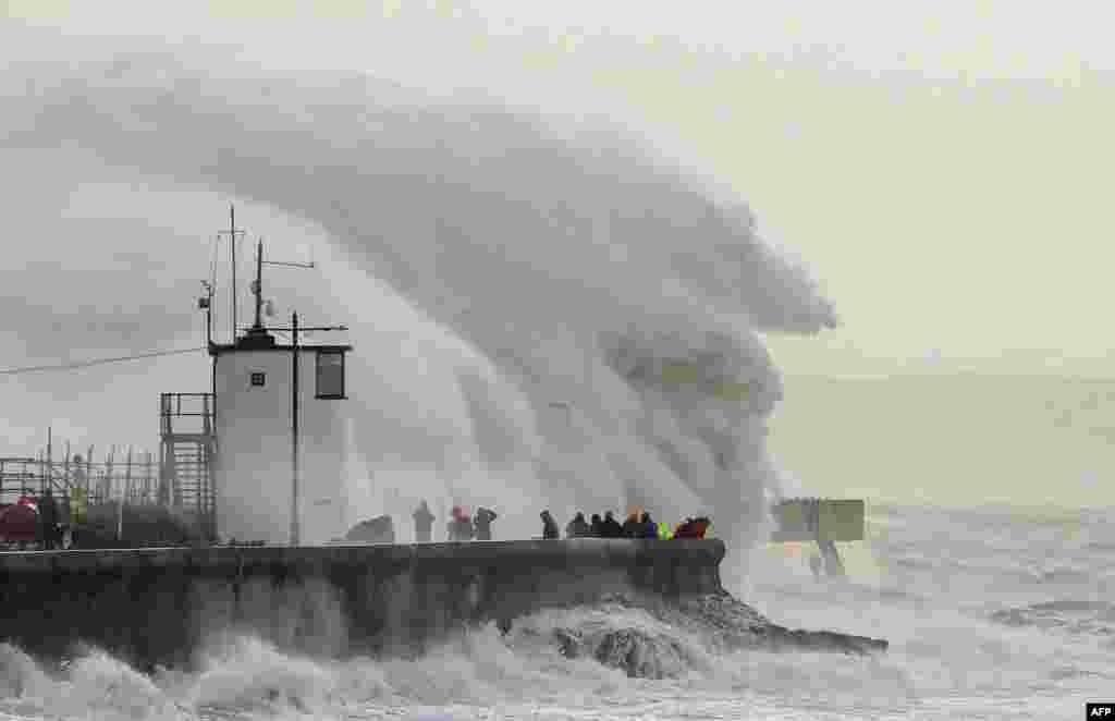 People watch as waves crash against the sea wall at Porthcawl, south Wales, as Storm Eunice brings high winds across the country. 