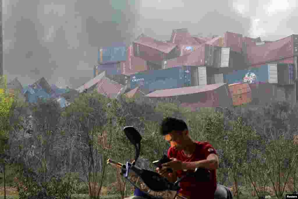 A man checks his mobile phone near shipping containers that were overturned by the force of two huge explosions in the Binhai district of Tianjin, Aug. 13, 2015.