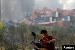 A man checks his mobile phone near shipping containers that were overturned by the force of two huge explosions in the Binhai district of Tianjin, China, August 13, 2015.