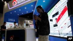FILE - In this Thursday, April 28, 2016 file photo, a woman browses her smartphone near a display booth for China's Weibo microblogging website at the 2016 Global Mobile Internet Conference (GMIC) in Beijing. Beijing (AP Photo/Andy Wong, File)