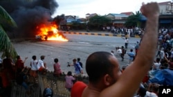 A Buddhist monk shouts as people gather to watch a burning military police car near a polling station in Phnom Penh, Sunday, July 28, 2013. 