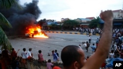 A Buddhist monk shouts as people gather to watch a burning military police car near a polling station in Phnom Penh, Cambodia, Sunday, July 28, 2013. 