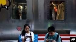 Shoppers sit on a bench with a decorated U.S. flag browsing their smartphones outside a fashion boutique selling U.S. brand clothing at the capital city's popular shopping mall in Beijing, Sept. 24, 2018. 