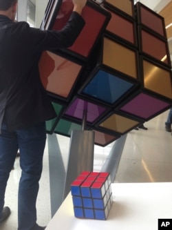 A traditional Rubik’s Cube sits on a podium in the foreground while a person operates an oversized version shortly after its unveiling inside the University of Michigan’s G.G. Brown engineering building in Ann Arbor, Mich., April 13, 2017.