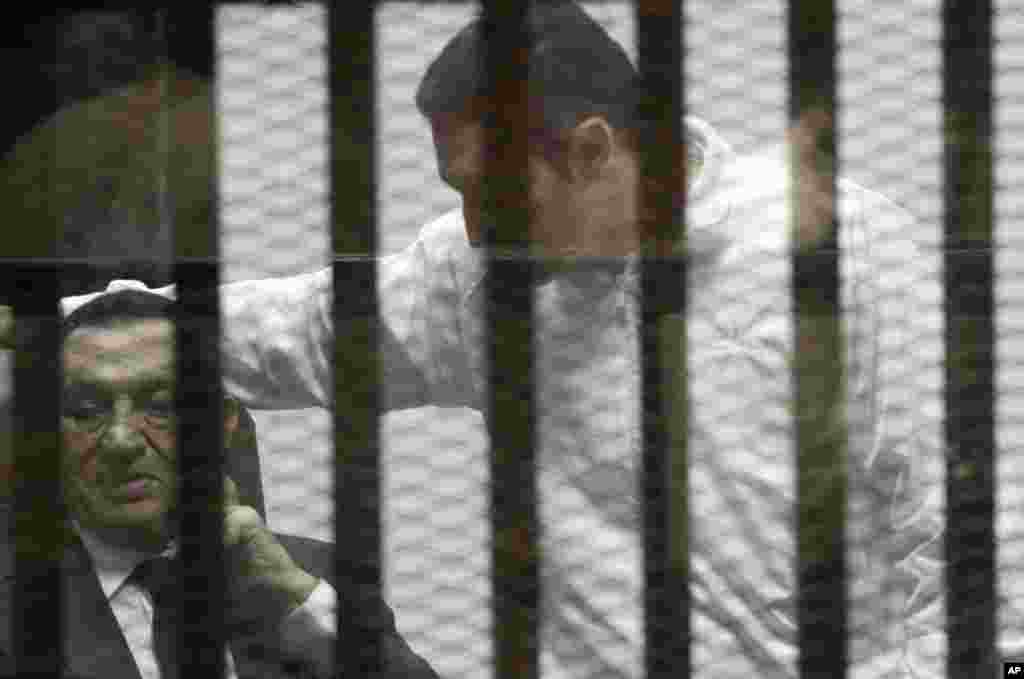 Ousted Egyptian president Hosni Mubarak, sits in a defendant cage with protective glass along side his son Alaa (right) during a court hearing in Cairo, May 21, 2014.