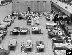In this 1918 photo made available by the Library of Congress, volunteer nurses from the American Red Cross tend to influenza patients in the Oakland Municipal Auditorium, used as a temporary hospital.