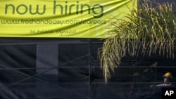Un trabajador de la construcción junto a un letrero que anuncia nuevas contrataciones en Los Angeles.