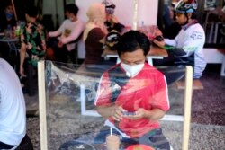 Seorang pria di sebuah warung kopi duduk di meja yang dibatasi pelindung plastik untuk mencegah penularan virus corona, di Makassar, Sulawesi Selatan, 31 Mei 2020. (Foto: AP)