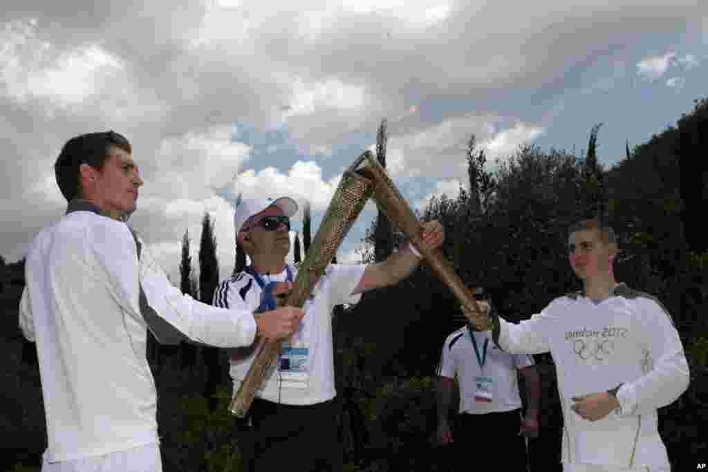 Second Olympic Torch bearer, Alex Loukos from Great Britain, right, receives the Olympic torch from Spyros Gianniotis, left.
