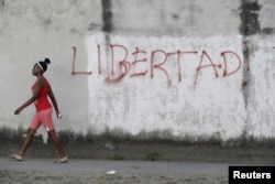FILE - A young woman walks near graffiti that reads "Freedom" in Havana, Feb. 21, 2016.