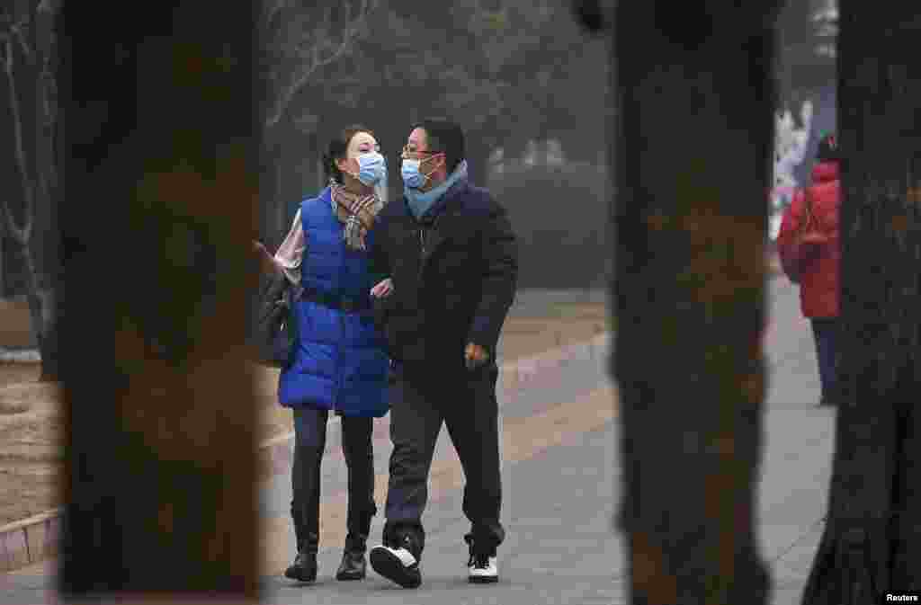 Pasangan mengenakan masker berjalan di suatu siang yang berkabut di Beijing, China.