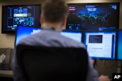 Security specialist Erik Dickmeyer works at a computer station with a cyber threat map displayed on a wall in front of him, May 20, 2015, in the Cyber Security Operations Center at AEP headquarters in Columbus, Ohio.