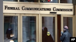 FILE - A person with a smart phone enters the Federal Communications Commission (FCC) in Washington, Dec. 14, 2017. 