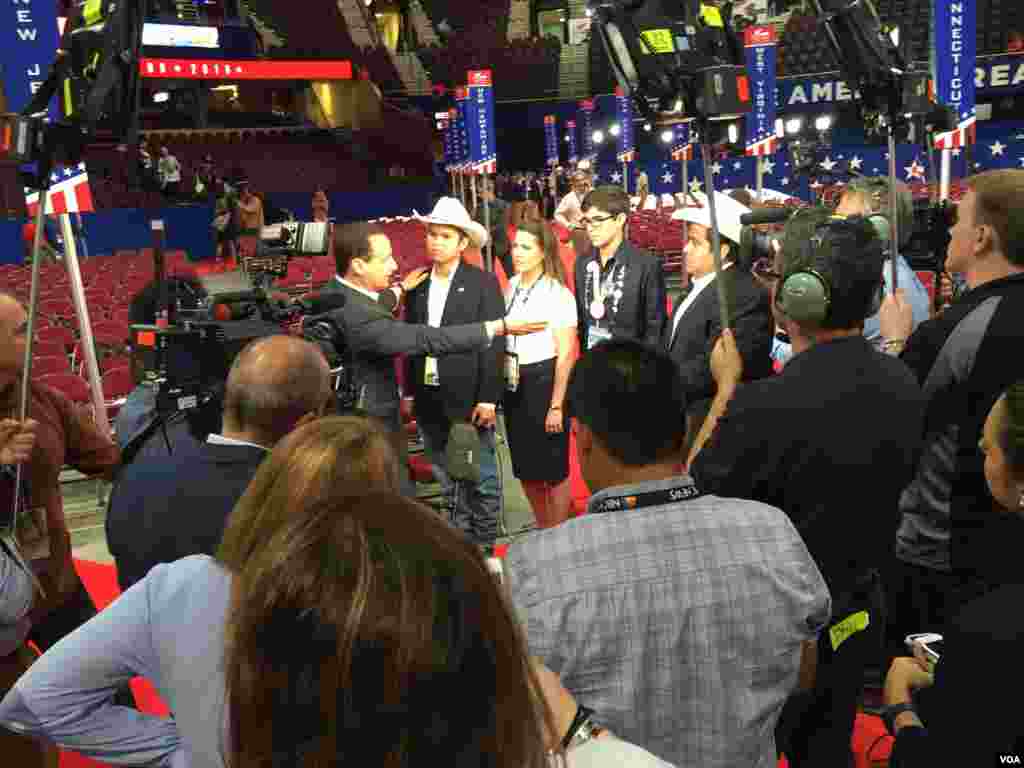 Four Hispanic delegates -- two from Texas, wearing hats, and two from Florida -- are interviewed by TV Telemundo on the floor at the Republican National Convention at Quicken Loans Arena, in Cleveland, July 19, 2016. (Photo: Mia Bush / VOA)