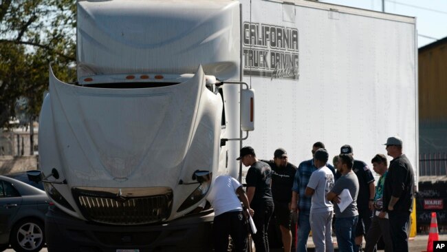 Student drivers gather around a practice truck to inspect the vehicle at California Truck Driving Academy in Inglewood, Calif., Nov. 15, 2021.