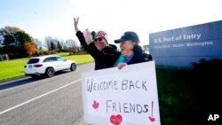 FILE - Dual U.S.-Canadian citizen Traysi Spring, right, and her American husband Tom Bakken, hold a homemade sign to welcome people heading into the U.S. from Canada, Nov. 8, 2021, in Blaine, Wash. The U.S. reopened its land borders to nonessential travel at that time after almost 20 months of COVID-19 restrictions. Now the U.S. has again discouraged travel to the north.