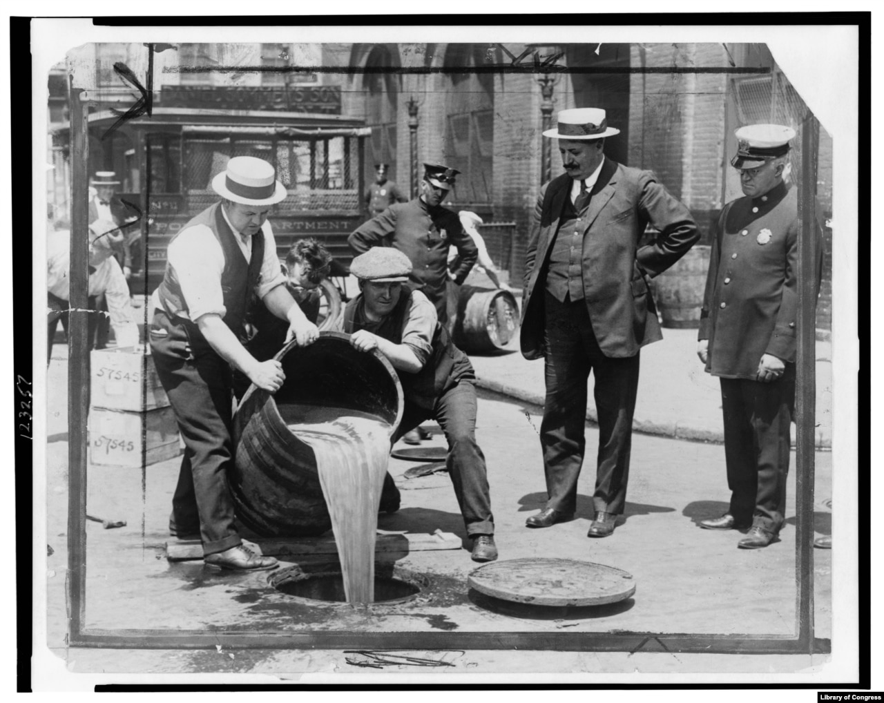 New York City Deputy Police Commissioner John A. Leach, right, watching agents pour liquor into sewer following a raid during the height of prohibition. (Library of Congress)}