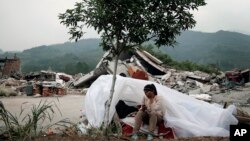 A child sits at a makeshift tent in front of homes destroyed by Saturday's earthquake in Longmen village in Lushan county of southwest China's Sichuan province, April 21, 2013. 