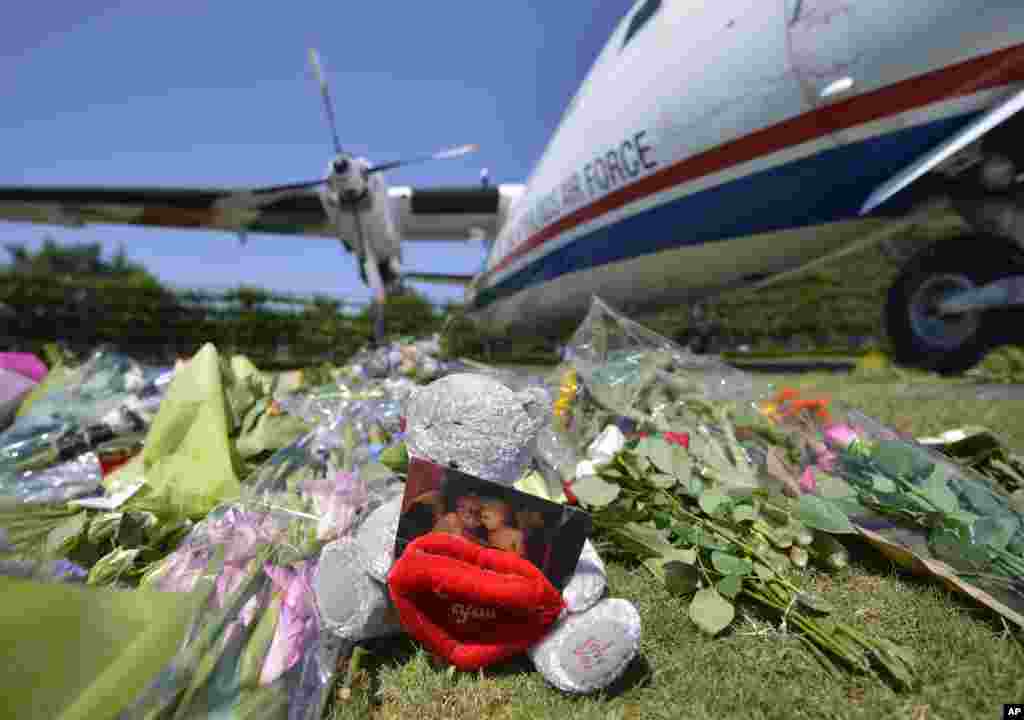 Bunga dan boneka beruang ditempatkan di depan sebuah pesawat sebelum upacara yang menandai kembalinya jenazah-jenazah pertama para penumpang dan awak yang tewas dalam jatuhnya pesawat Malaysia Airlines MH17, di markas militer Eindhoven (23/7). (AP/Martin Meissner)