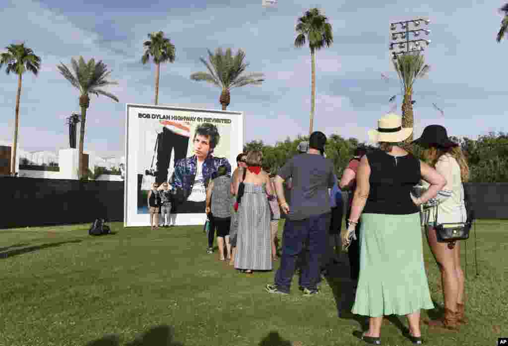 Festival goers wait in line to be photographed against a billboard of Bob Dylan's album "Highway 61 Revisited" on day 1 of the 2016 Desert Trip music festival at Empire Polo Field, Oct. 7, 2016, in Indio, California.