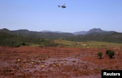 FILE - A helicopter flies over the Bento Rodrigues district, covered with mud after a dam owned by Vale SA and BHP Billiton Ltd burst in Mariana, Brazil, Nov. 6, 2015.