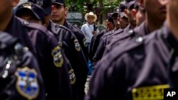 FILE - A man looks at a formation of police and soldiers during a presentation to the press in the Central Square in San Salvador, El Salvador, June 14, 2016.