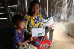 Kea Teav and her son hold a 'poverty' identification card given to her by the commune authority in Krakor district, Pursat province, Cambodia, August 5, 2020. (Sun Narin/VOA Khmer)