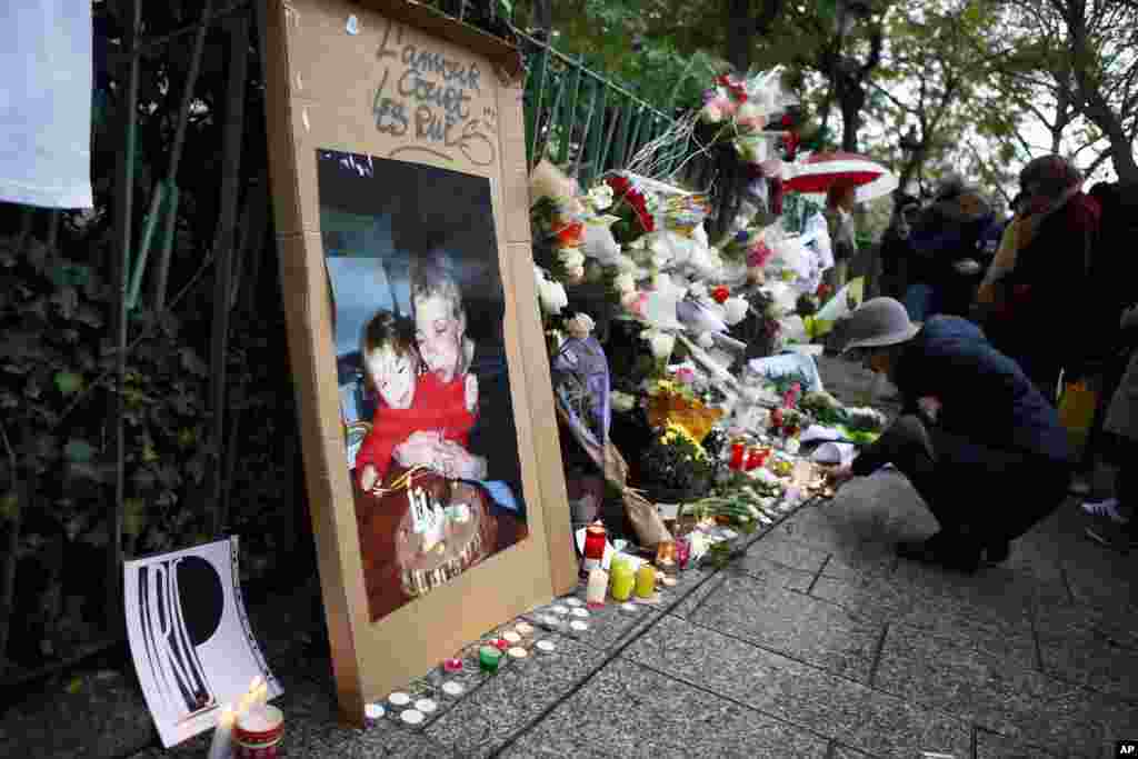 Seorang perempuan menyalakan lilin-lilin untuk menghormati para korban serangan maut di Paris tahun lalu, di depan gedung konser Bataclan (13/11). (AP/Francois Mori)