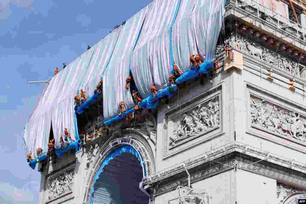 Workers unravel silver blue fabric, part of a process of wrapping L&#39;Arc de Triomphe in Paris, France, designed by the late artist Christo.