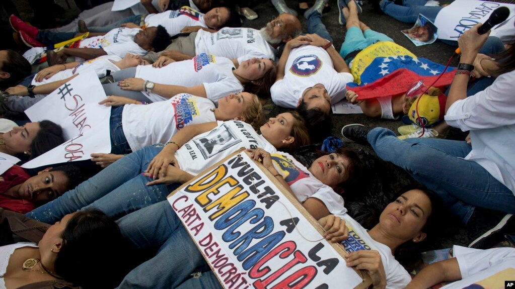 FILE - Opposition supporters lie on the ground during a demonstration outside of the Organization of American States, OAS, office building, in Caracas, Venezuela, June 23, 2016.