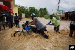 Men push a motorbike through a street flooded by a river that overflowed from heavy rains caused by Hurricane Matthew in Leogane, Haiti, Oct. 5, 2016.