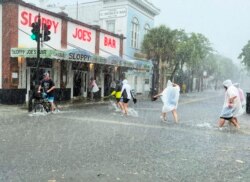 Pengunjung berjalan menuju Sloppy Joe's Bar, melintasi Duval Street yang banjir akibat angin kencang dan hujan melewati Key West, Florida, Selasa, 6 Juli 2021. (AP)