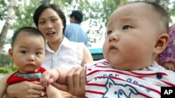 FILE - Two Chinese babies sit with their mothers in a Beijing park, July 10, 2003. 
