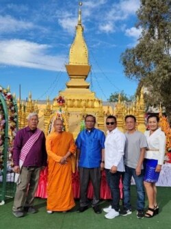 ​ຊາວ​ລາວ​ແລະ​ຄູ​ບາ​ຖ່າຍ​ຮູບ​ຢູ່​ຕໍ່​ໜ້າ​ພະທາດຫລວງ​ຈຳ​ລອງຢູ່​ວັດບຸດດາຣັດຕະນະຣາມທີ່​ສ້າງ​ໃໝ່​ຢູ່​ນະ​ຄອນ​ຟີ​ນິກ