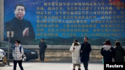 FILE - People walk in front of a poster featuring a portrait of Chinese President Xi Jinping, in Beijing, China, Feb. 26, 2018. 