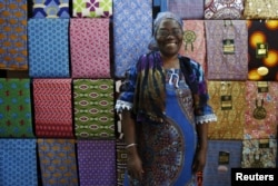 FILE - Fofanan Man, a 59-year-old businesswoman, poses for a photograph in front of textiles in her shop in Bouake, Ivory Coast, Feb. 10, 2016.